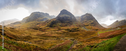 Panoramic view of steep mountains in the center and valleys on both sides with bright green and orange on an overcast afternoon in Glencoe, Highland, Scotland, United Kingdom photo