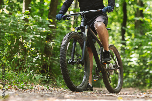 Sporty body of young cyclist riding bike down the woods
