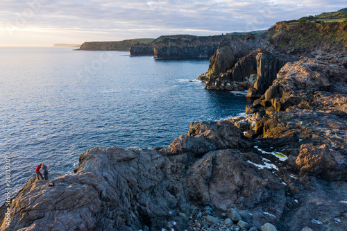 Two photographers take pictures of the sunrise at the rocky coastline of Ponta do Mistério at Terceira Island