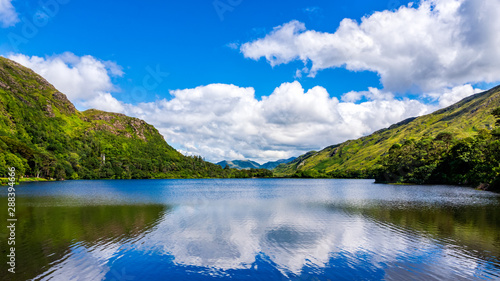 Fototapeta Naklejka Na Ścianę i Meble -  Beautiful shot of a tranquil lake and mountain with puffy clouds reflected in water. Scenic green meadows and hills of Connemara, Ireland