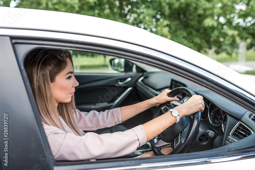 Beautiful business woman lady driving a car, right-hand drive, left-hand traffic, summer in the city, background of trees and foliage. A strict pink suit watches on his hands. © byswat