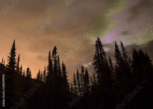 Aurora (Northern Lights) and stars over a calm forested mountain scene with orange, purple and green clouds.