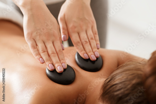 Relaxed woman getting stones shoulder massage in spa