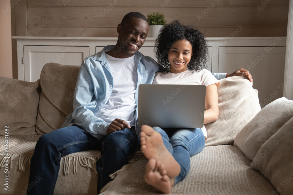 Happy biracial couple relax on couch using laptop Happy biracial couple relax on couch using laptop