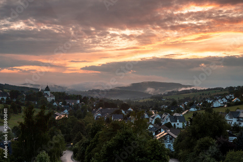 Panoramic view over the mountainous village of Grafschaft in the winter sports region of Sauerland  Germany  during a colourful orange lit cloudy sky