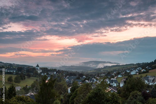 Mountainous village of Grafschaft in the winter sports region of Sauerland, Germany, during a colourful orange lit cloudy sky at sunset