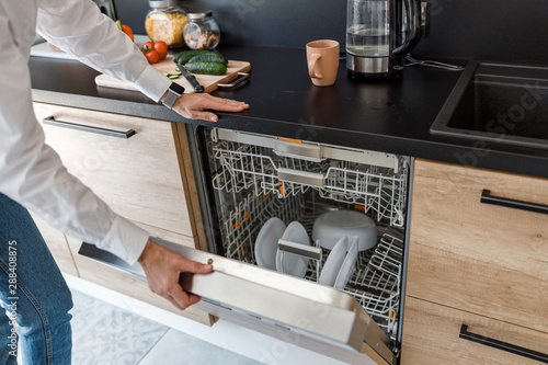 Woman is opening the dishwasher in the kitchen photo