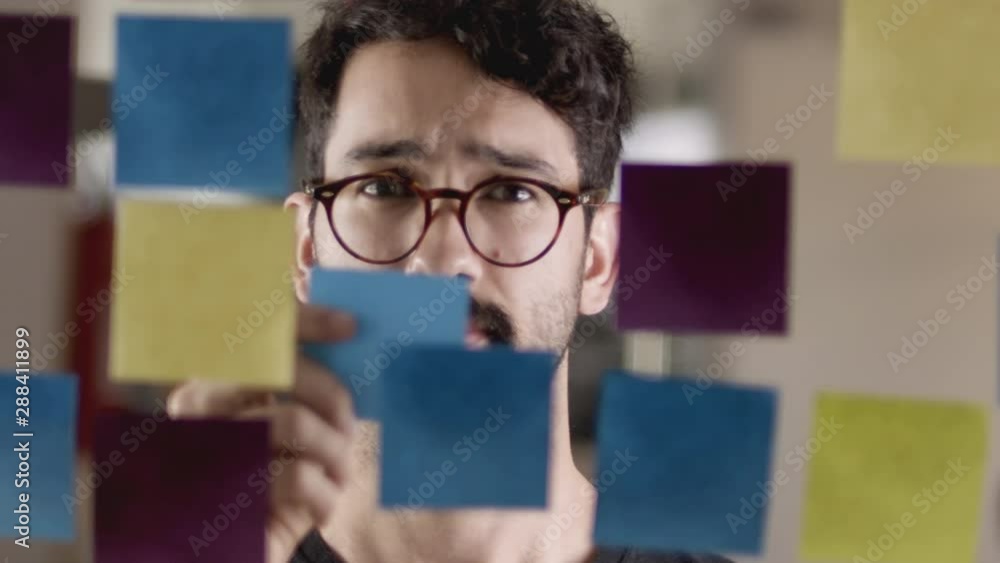 Close up of a young man brainstorming and placing a sticky note on a glass whiteboard. Close up of a young man brainstorming and placing a sticky note on a glass whiteboard.