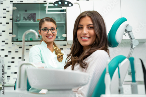 Pretty woman with perfect smile siting in dentist chair and looking at camera  dentist in background. focus on dentist 