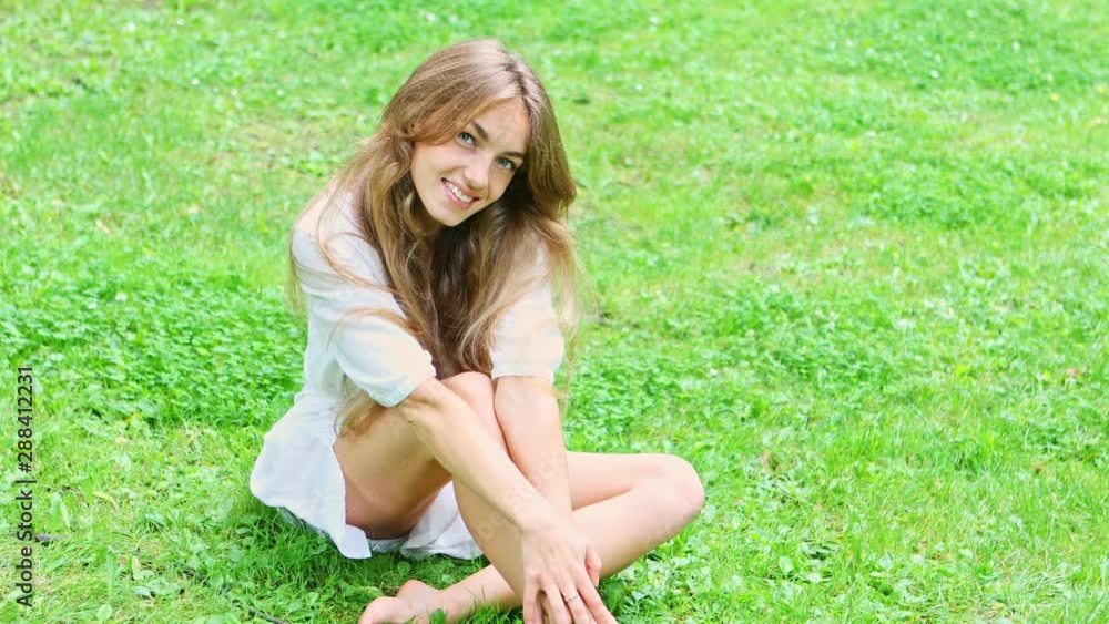 Gorgeous young woman in white dress sitting on the green lawn while she is posing and looking seducing into the camera Gorgeous young woman in white dress sitting on the green lawn while she is posing and looking seducing into the camera