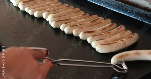 Grilled sausages on hot bbq black steel flat grill plate. Hand flip, pinch and fried  white pork and veal sausage, Wollwurst, on hot plate.  photo