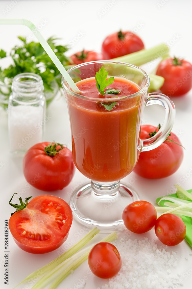 Tomato juice is poured into a transparent glass with parsley and herring, on a white background with cherry tomatoes, lit by sunlight Tomato juice is poured into a transparent glass with parsley and herring, on a white background with cherry tomatoes, lit by sunlight