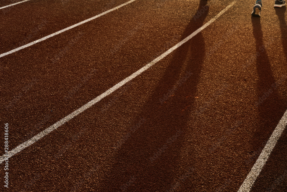 shadow of running people for exercise on the red and white line track floor of sport field in the morning sunrise background