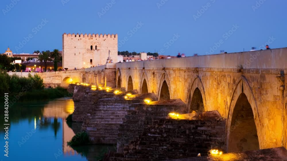Cordoba, Spain. Roman bridge across the Guadalquivir river and Calagorra Tower at sunset with people walking on them in Cordoba, Andalusia, Spain. Time-lapse in the evening with clear sky Cordoba, Spain. Roman bridge across the Guadalquivir river and Calagorra Tower at sunset with people walking on them in Cordoba, Andalusia, Spain. Time-lapse in the evening with clear sky