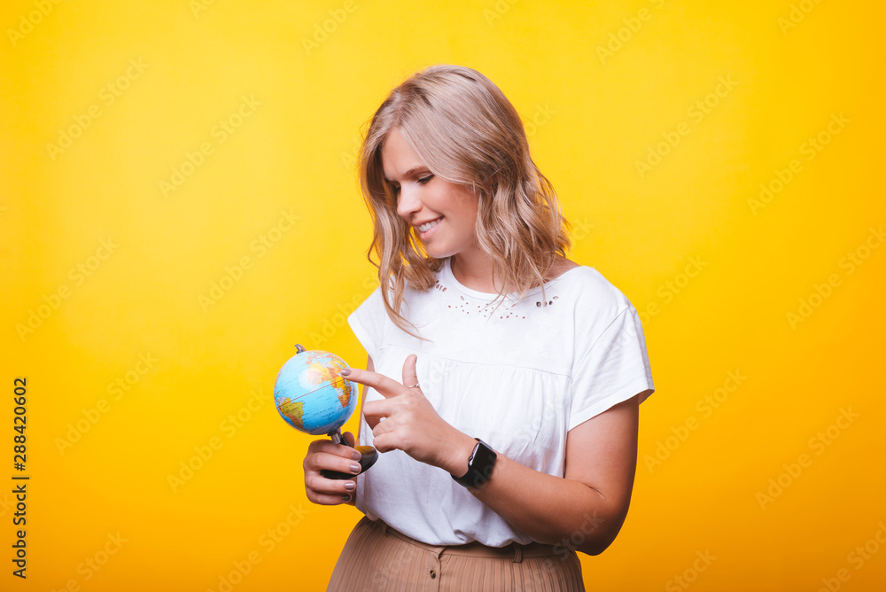 Handsome young blonde woman, pointing at globus over yellow wall Handsome young blonde woman, pointing at globus over yellow wall
