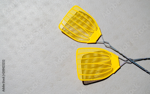 two crossed yellow fly swatters on a gray plastic picnic table with copy space photo