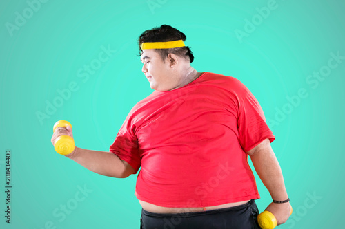 Overweight man exercises biceps with dumbbells © Creativa Images