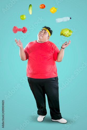 Overweight man juggling dumbbell and foodstuff © Creativa Images