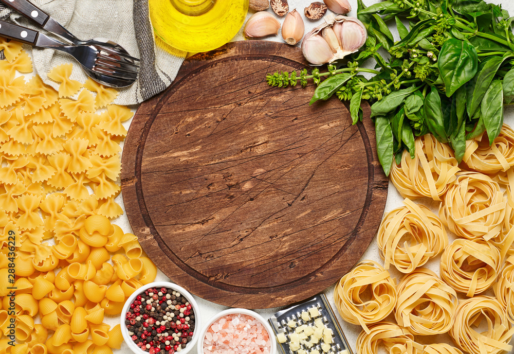 Round rustic wooden cutting board surrounded by different types of Italian pasta