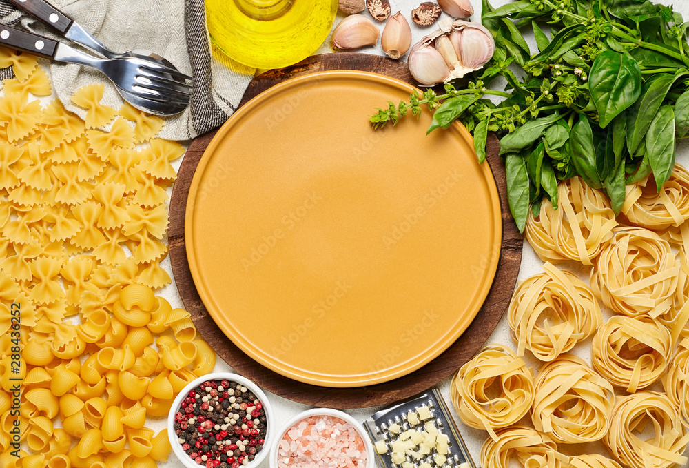 Yellow plate surrounded by different types of Italian pasta, fresh basil, olive oil, garlic and mozzarella cheese