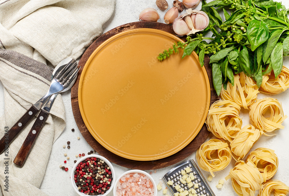 Yellow plate surrounded by different types of Italian pasta, fresh basil, garlic and mozzarella cheese