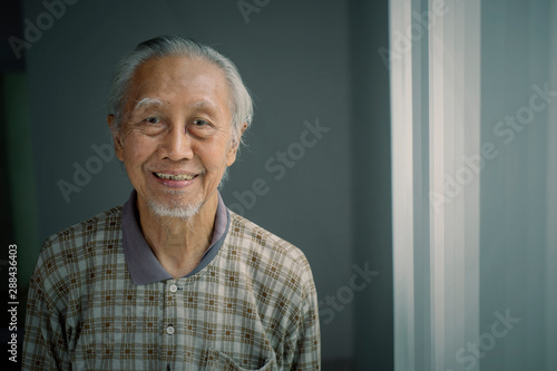 Fotografiet Smiling elderly man standing near the window