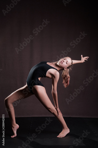 A girl in a black swimsuit performs exercises on flexibility, ballet, yoga, gymnastics.
