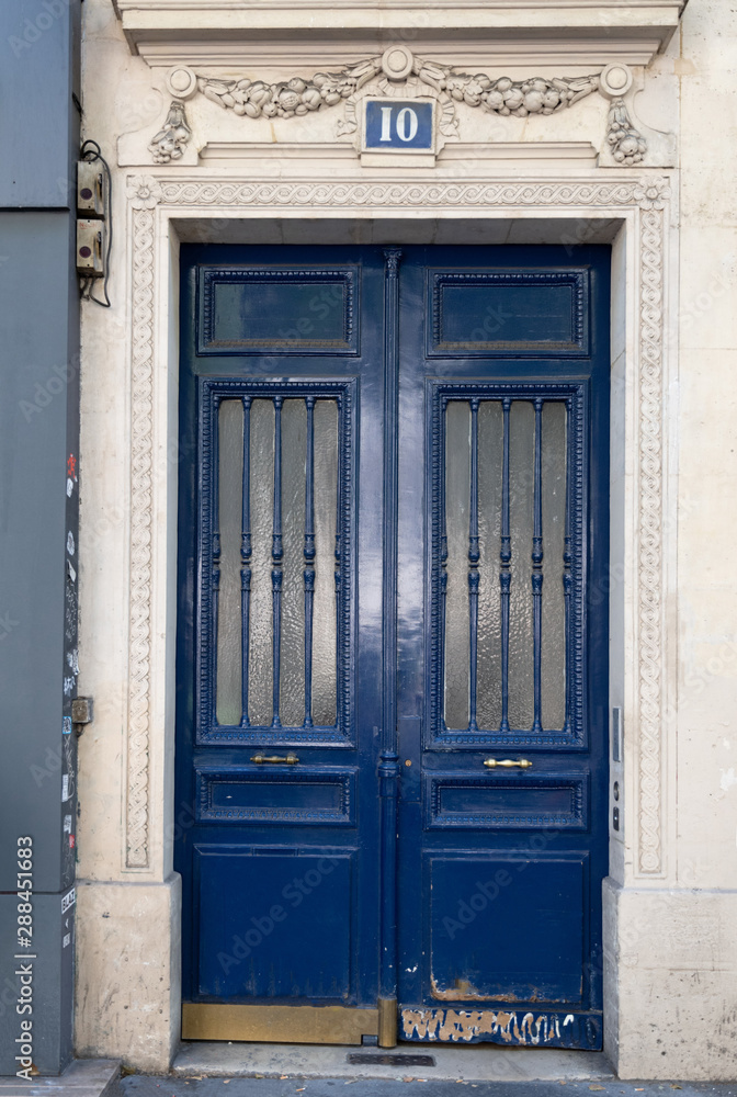 Old wooden door. Paris / France - 06 26 2019: Doorway with door windows with matte glass protected by vertical patterned grids. Dark blue painted antique door with shabby bottom part. Antique building