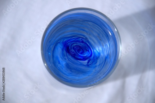 Stains of blue ink in water in a transparent glass on a white 