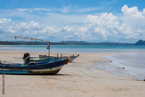Side view of a wooden fishing boat on tropical beach with white sand and blue sky