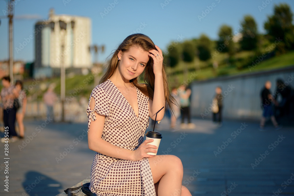 beautiful girl with coffee in hand sits on a bench on the street