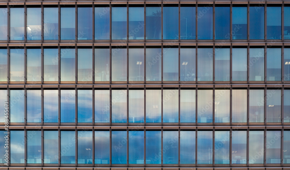 Detail of an office building with clouds reflecting in the glass facade