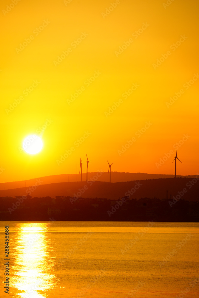 silhouetted windmills on hill over orange colored sunrise sky