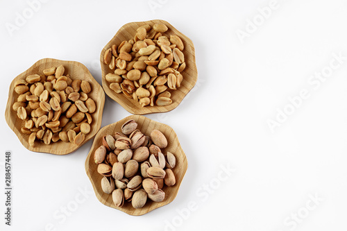 wood plates of salted peanuts and pistachios on white background. snack to beer