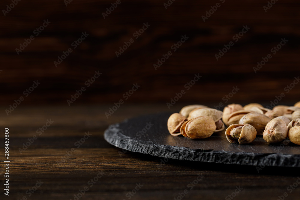 salted pistachio nuts on stone board on wood background. salted pistachio nuts on stone board on wood background.