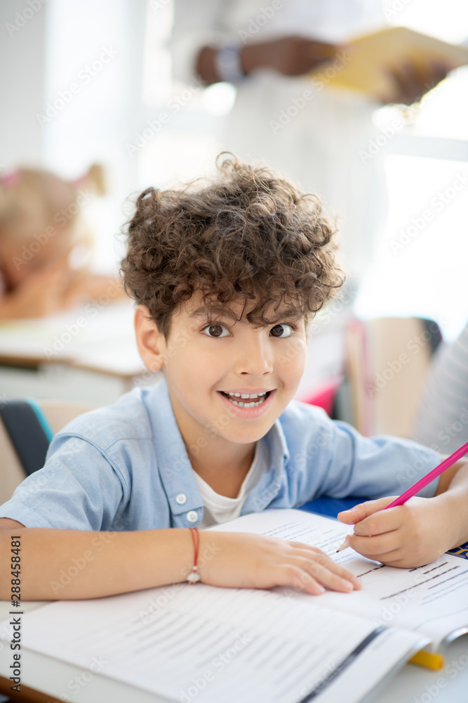 Dark-eyed schoolboy making funny face while writing Dark-eyed schoolboy making funny face while writing