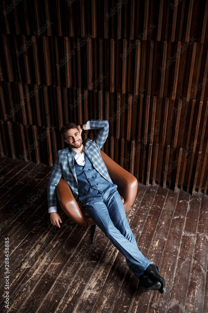 Young successful businessman in a blue suit in a cage is sitting in a leather chair. young man with a beard smiling. Young successful businessman in a blue suit in a cage is sitting in a leather chair. young man with a beard smiling.