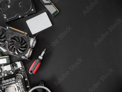 top view of computer parts with harddisk, solid state drive, ram, CPU, graphics card, and motherboard on black table background.