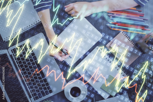 Financial forex graph drawn over hands taking notes background. Concept of research. Double exposure