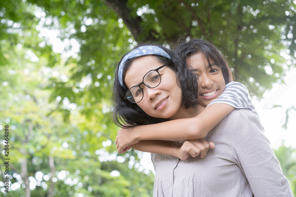 Cute Asian mother and daughter playing and giving ride on back together at park, Happy family concept Cute Asian mother and daughter playing and giving ride on back together at park, Happy family concept