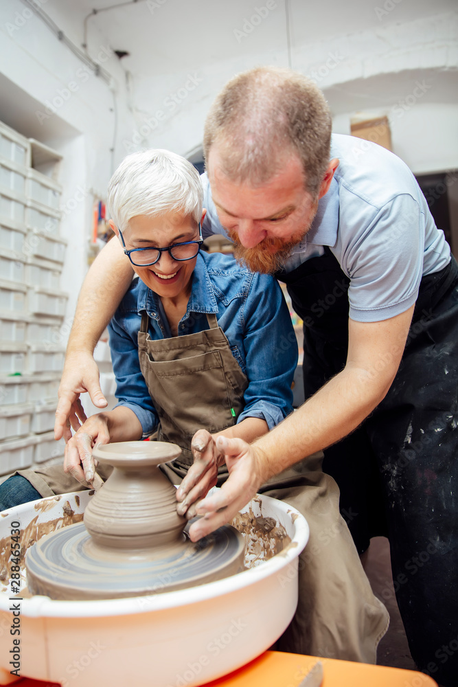 Senior woman spinning clay on a wheel with teacher at pottery class Senior woman spinning clay on a wheel with teacher at pottery class