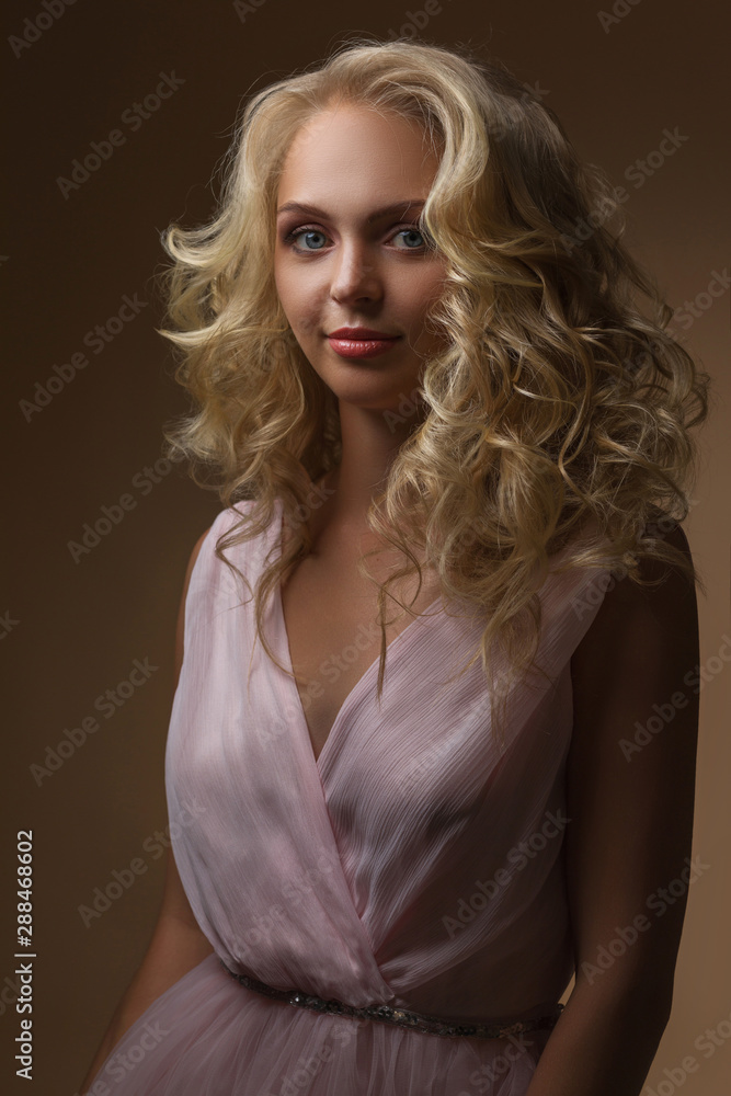 Naklejka premium portrait of beautiful curly blonde woman in gorgeous pink dress looking at camera