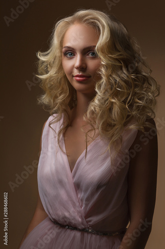 portrait of beautiful curly blonde woman in gorgeous pink dress looking at camera