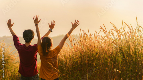 Asian woman and man standing and hand up in meadow and looking far away at sunrise time, Selective focus.; 