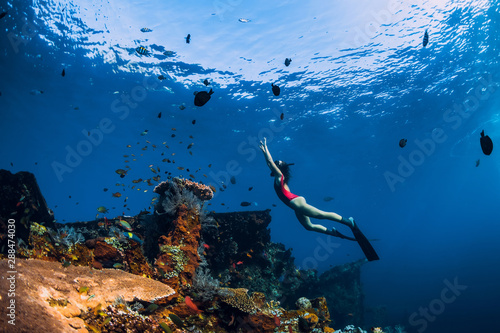 Free diver woman swimming with fins at wreck ship. Freediving in ocean over corals