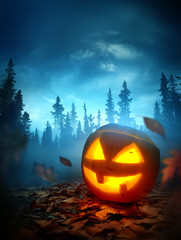 A halloween background with a glowing spooky Jack O Lantern pumpkin outside at night with a forest in the background. Photo composite.