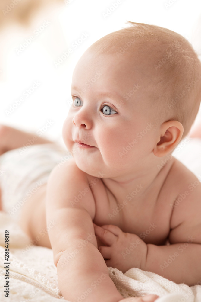 Happy little baby girl infant on a bed in white bedroom near the bright window Happy little baby girl infant on a bed in white bedroom near the bright window