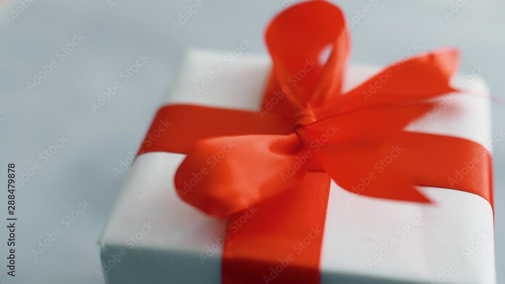 White gift box with red silk ribbon rotating on texture surface. Gift box for Christmas, black friday and other holidays. Close up 4k footage. White gift box with red silk ribbon rotating on texture surface. Gift box for Christmas, black friday and other holidays. Close up 4k footage.