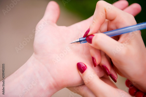 the girl is going to write to the guy on his hand her phone number with a blue pen