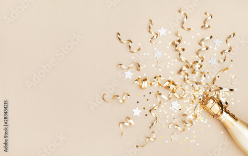 Champagne bottle with confetti stars and party streamers on gold festive background. Christmas  birthday or wedding concept. Flat lay.